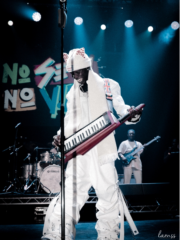 Seyi Vibez in a white outfit playing a red keytar during a live concert with blue overhead lighting. — concert photography London by Lamss Media